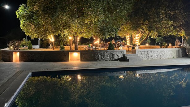 Zona de piscina a l'aire lliure amb seients de pedra i arbres, envoltada de camins ben il·luminats.