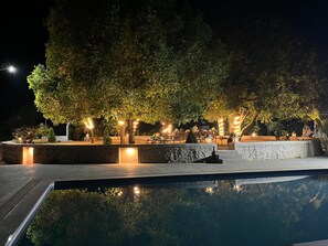 Un área de piscina al aire libre con asientos de piedra y árboles, rodeada de senderos bien iluminados.