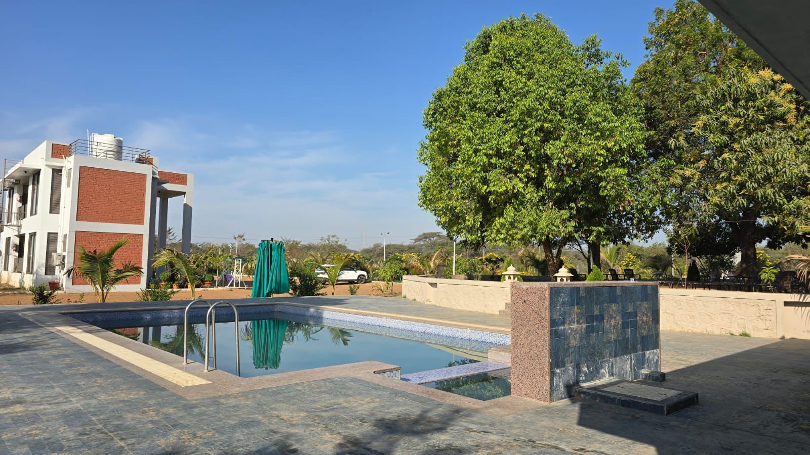 Une piscine à l’eau d’un bleu cristallin, entourée d’une zone pavée, d’un mur en pierre et d’un grand arbre qui offre de l’ombre.