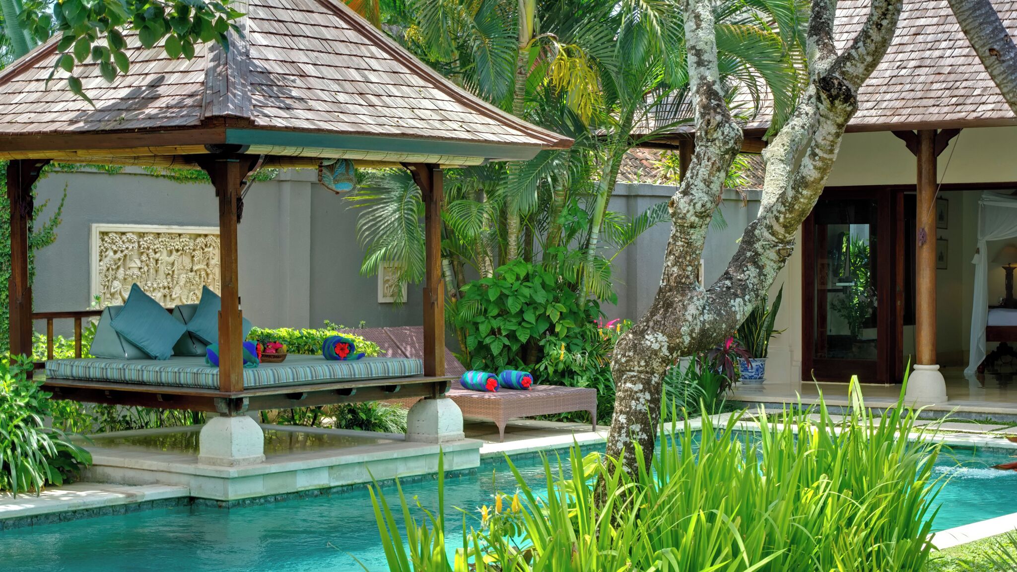 A poolside area with a covered seating area, lush greenery, and a clear view of the pool.