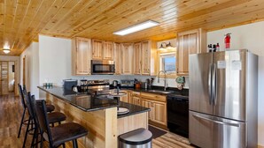 Una cocina moderna con armarios de madera, electrodomésticos de acero inoxidable y una zona de bar con taburetes.