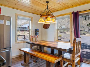 Una cucina rustica con un tavolo e una panca in legno, ampie finestre e un lampadario a sospensione.