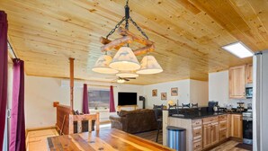 Un acogedor interior de cabaña con una mesa de comedor de madera, un sofá, una zona de cocina y un ventilador de techo.