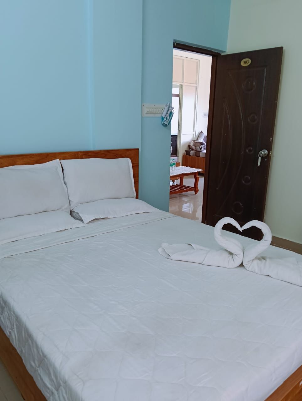 A neatly made bed with white linens and two towels arranged in a heart shape on the bed.