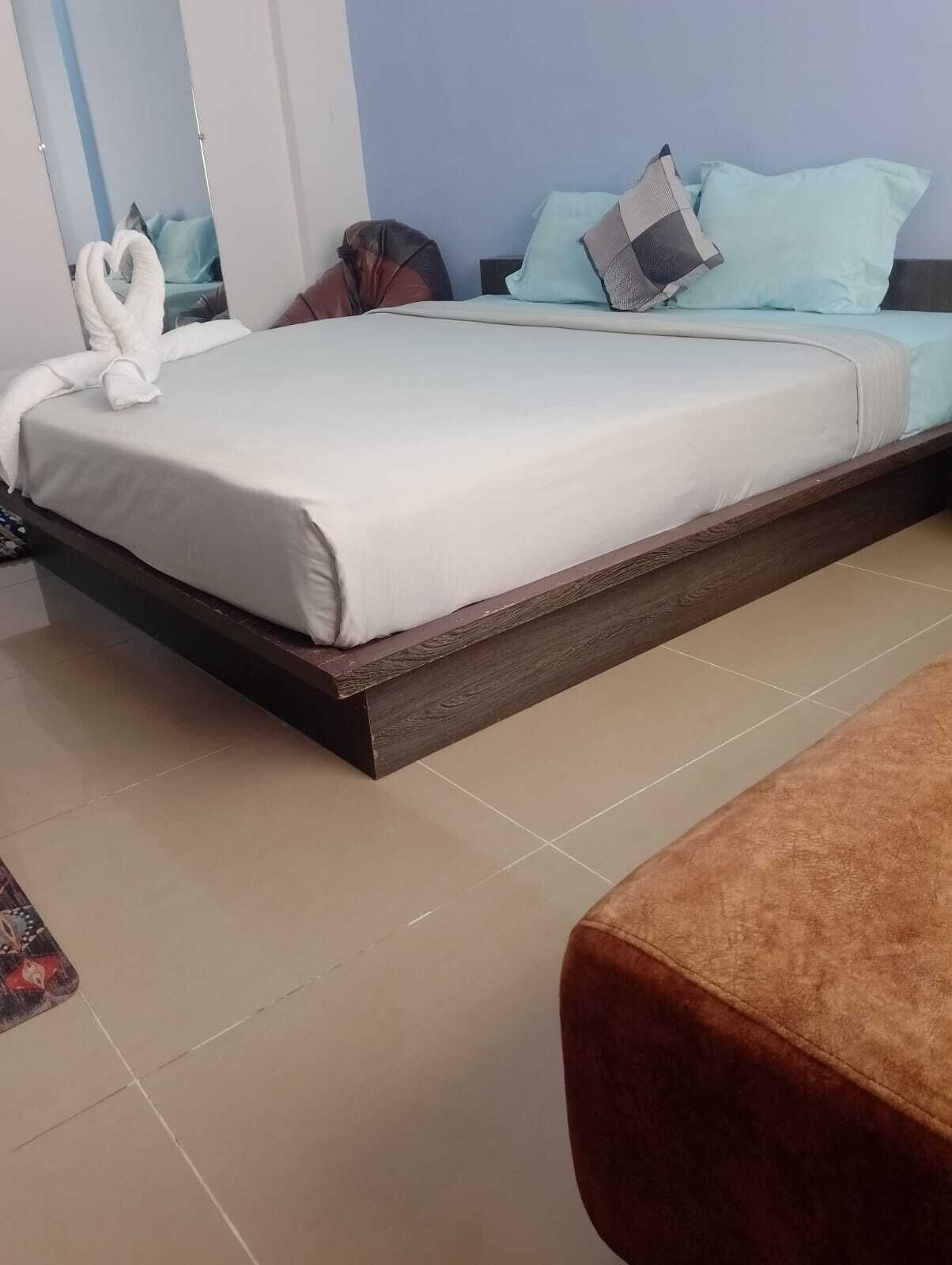 Ein ordentlich bezogenes Bett mit einer weißen Decke und einem herzförmigen Handtuch daneben.