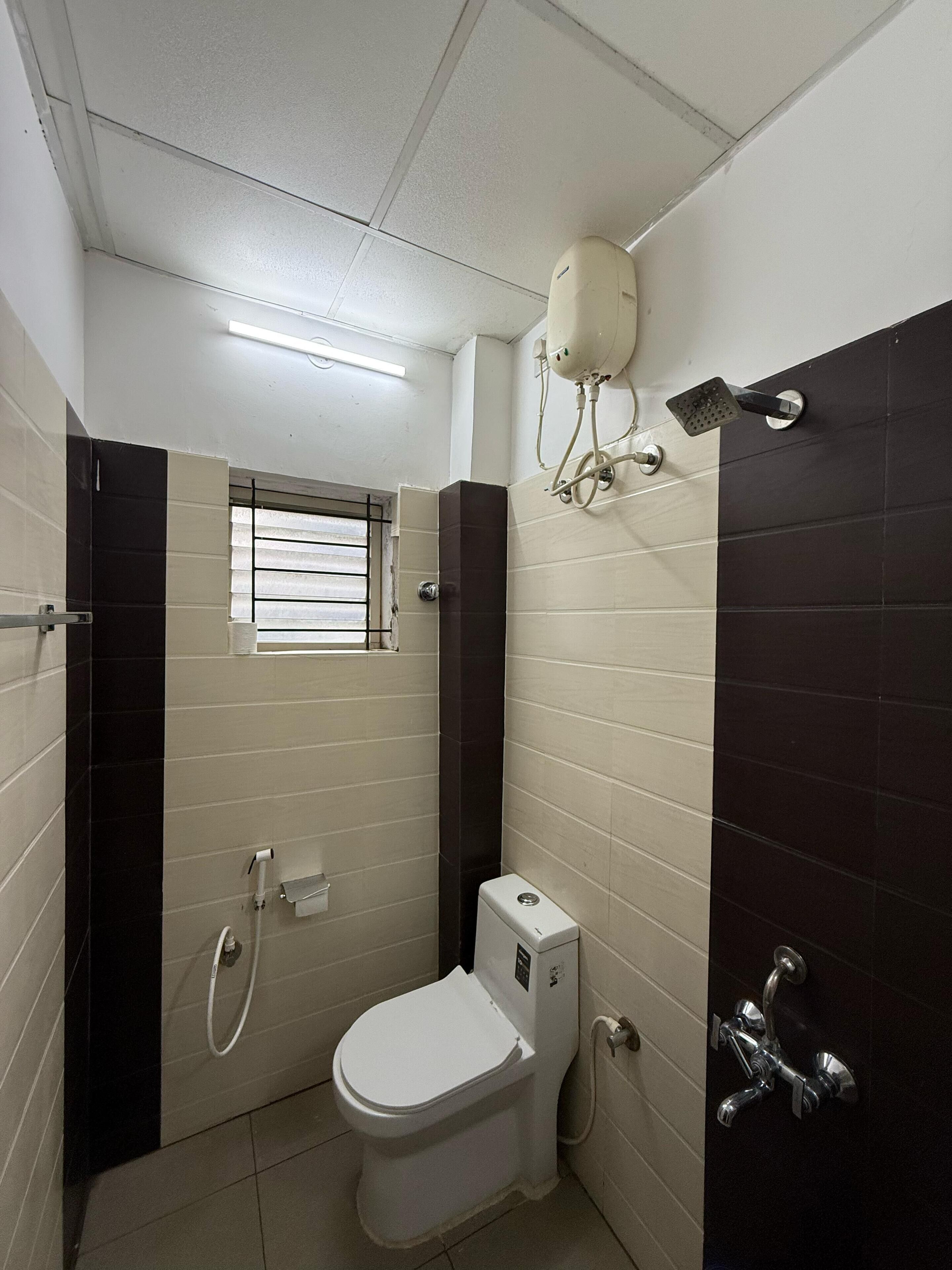 A compact bathroom with a toilet, a shower, and a window.