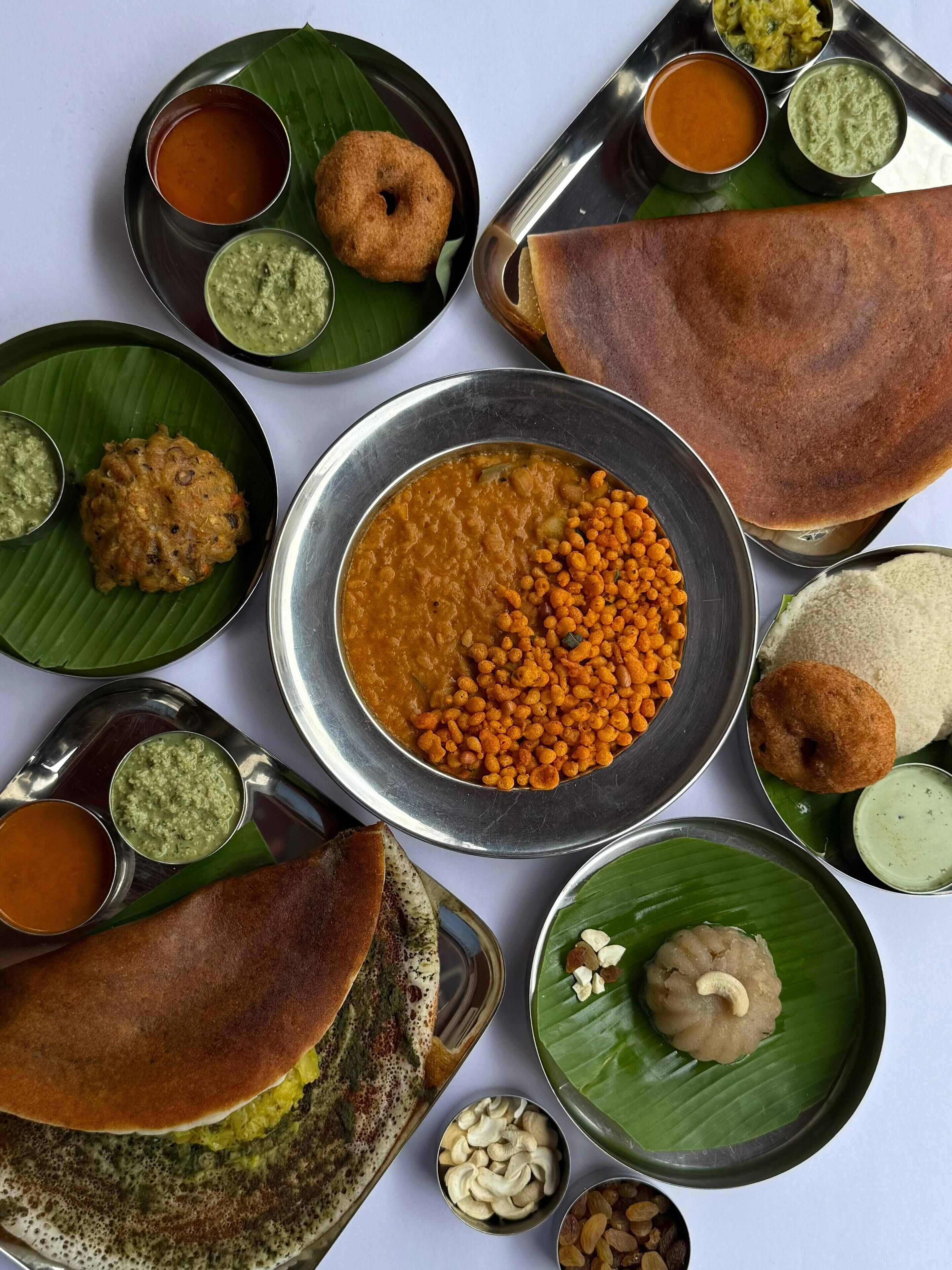 A variety of South Indian dishes arranged on metal plates and banana leaves.