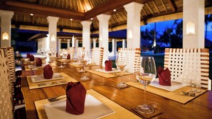 A restaurant with wooden tables set for dining, white chairs, and a view of the ocean at dusk. - Villa Sepoi Sepoi by Elite Havens (Lombok Utara)