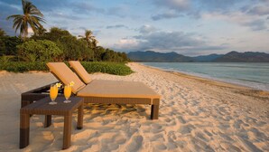 A beach with lounge chairs and a table with drinks, surrounded by greenery and mountains in the background. - Villa Sepoi Sepoi by Elite Havens (Lombok Utara)