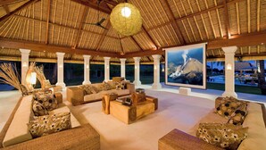 A spacious outdoor lounge area with comfortable seating, a large artwork depicting a volcano, and a thatched roof structure. - Villa Sepoi Sepoi by Elite Havens (Lombok Utara)