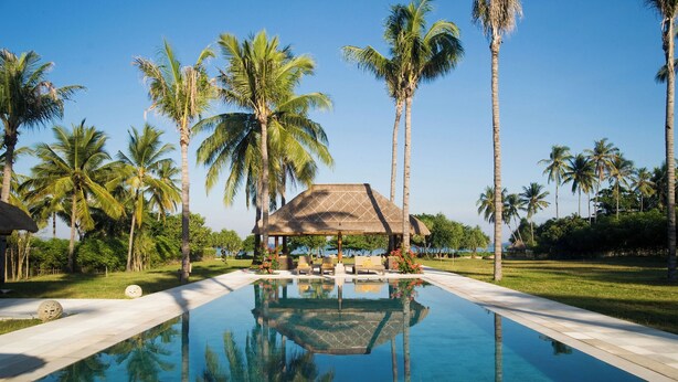 A swimming pool with a thatched-roof structure in the center, surrounded by palm trees and a clear sky. - Villa Sepoi Sepoi by Elite Havens (Lombok Utara)