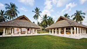 Two thatched-roof structures with open verandas, surrounded by palm trees and a well-maintained lawn. - Villa Sepoi Sepoi by Elite Havens (Lombok Utara)