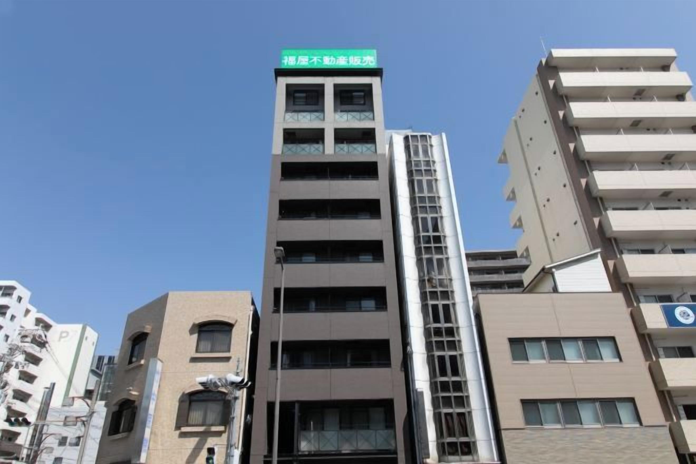A multi-story building with a prominent green sign at the top, several windows, and a visible fire escape.