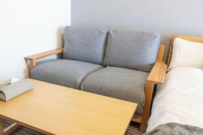 A room with a grey sofa, a wooden table, and a bed with white bedding.