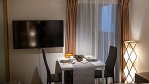 A hotel room with a flat-screen TV mounted on the wall, a dining table set with plates, glasses, and cutlery, and a floor lamp. - F・CROSS・EBISU (Osaka)