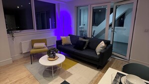 A modern living room with a sofa, coffee table, and dining area. - Modern 3 Bed Wembley Stadium View Apartment (Wembley)