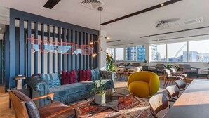 A modern office space with a blue and gray striped wall, a large sofa, a yellow chair, and a dining area with a long table. - Modern 3 Bed Wembley Stadium View Apartment (Wembley)