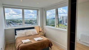 A bedroom with a large bed, two windows, and a view of the city. - Modern 3 Bed Wembley Stadium View Apartment (Wembley)