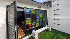 Un espace extérieur moderne doté d’une porte-fenêtre coulissante qui donne sur une pièce agrémentée de panneaux de verre colorés.