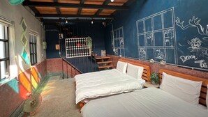 Une chambre avec deux lits, une petite table, une fenêtre et un mur recouvert d’un tableau noir où sont dessinés des motifs.