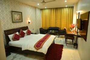 A hotel room with a bed, two chairs, a desk with a mirror, a TV, and a vase with flowers.
