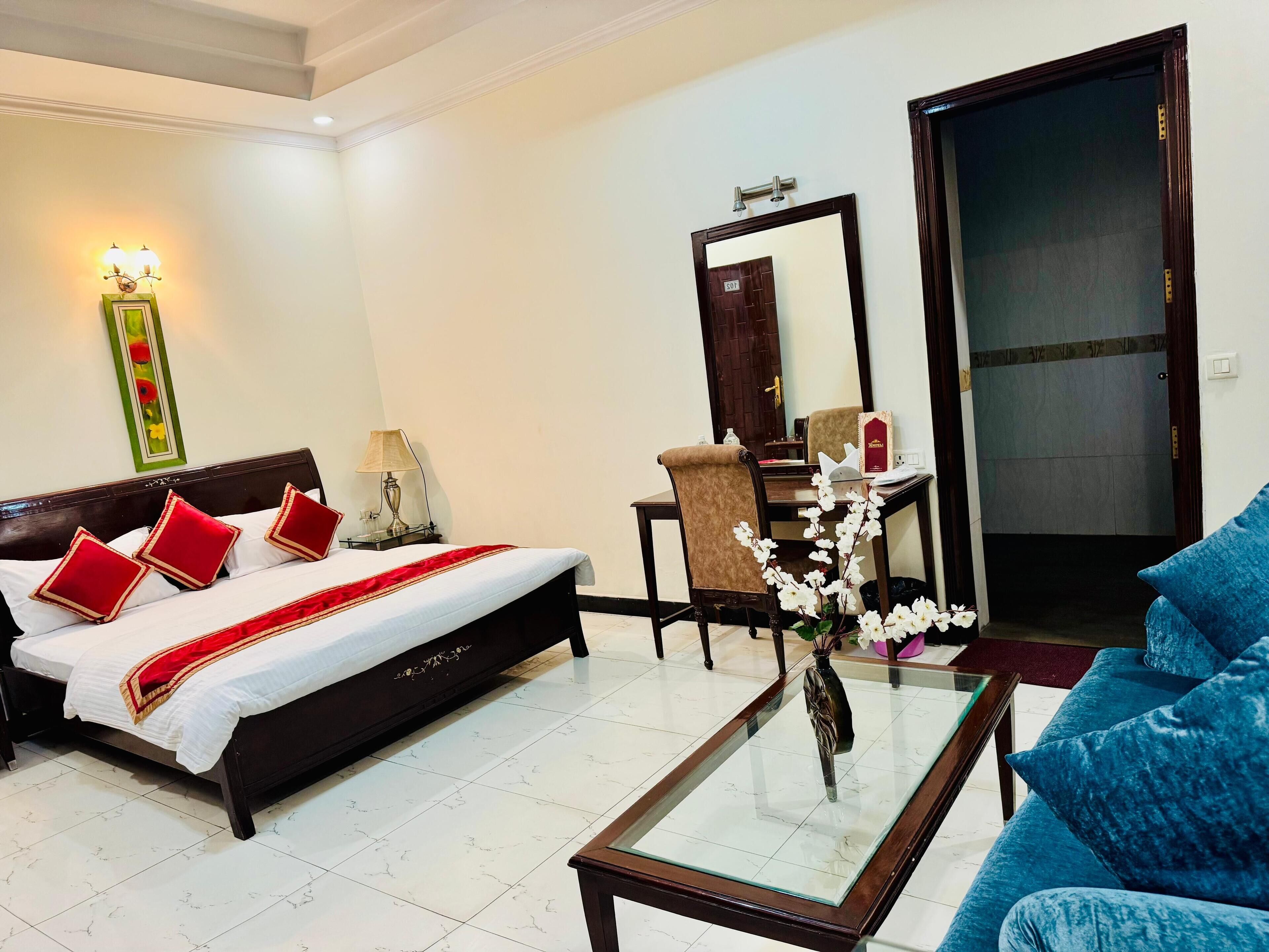 A hotel room with a bed, a desk, a chair, a sofa, and a glass coffee table.