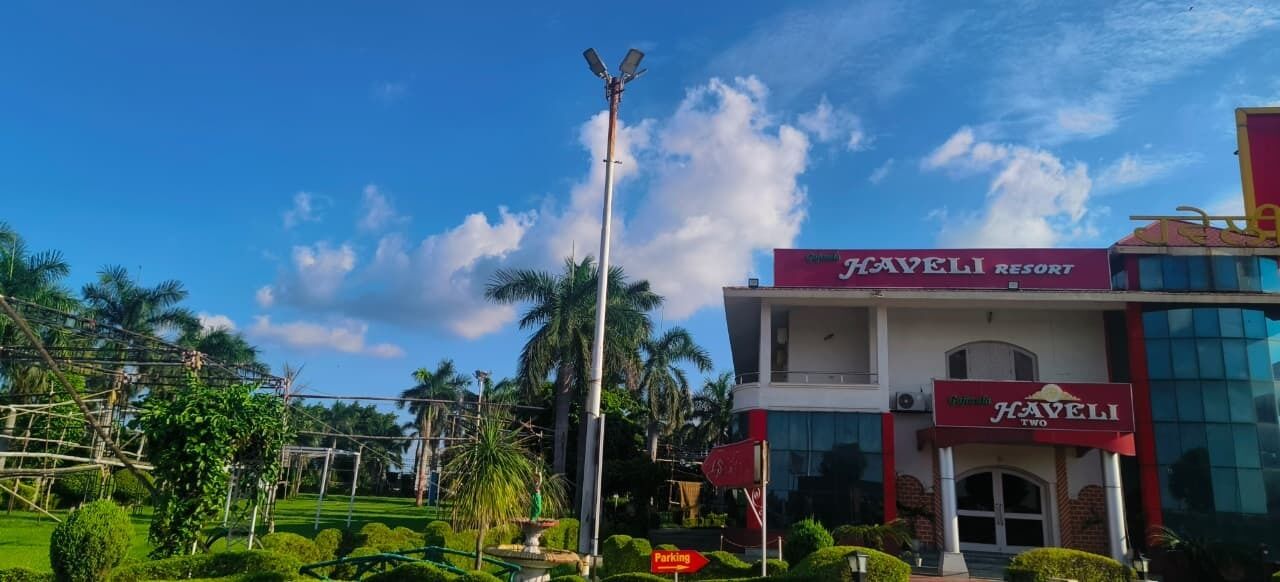 Un edificio con un cartel anunciando Haveli Resort, que presenta un estilo arquitectónico moderno con ventanas de vidrio y fachada roja.