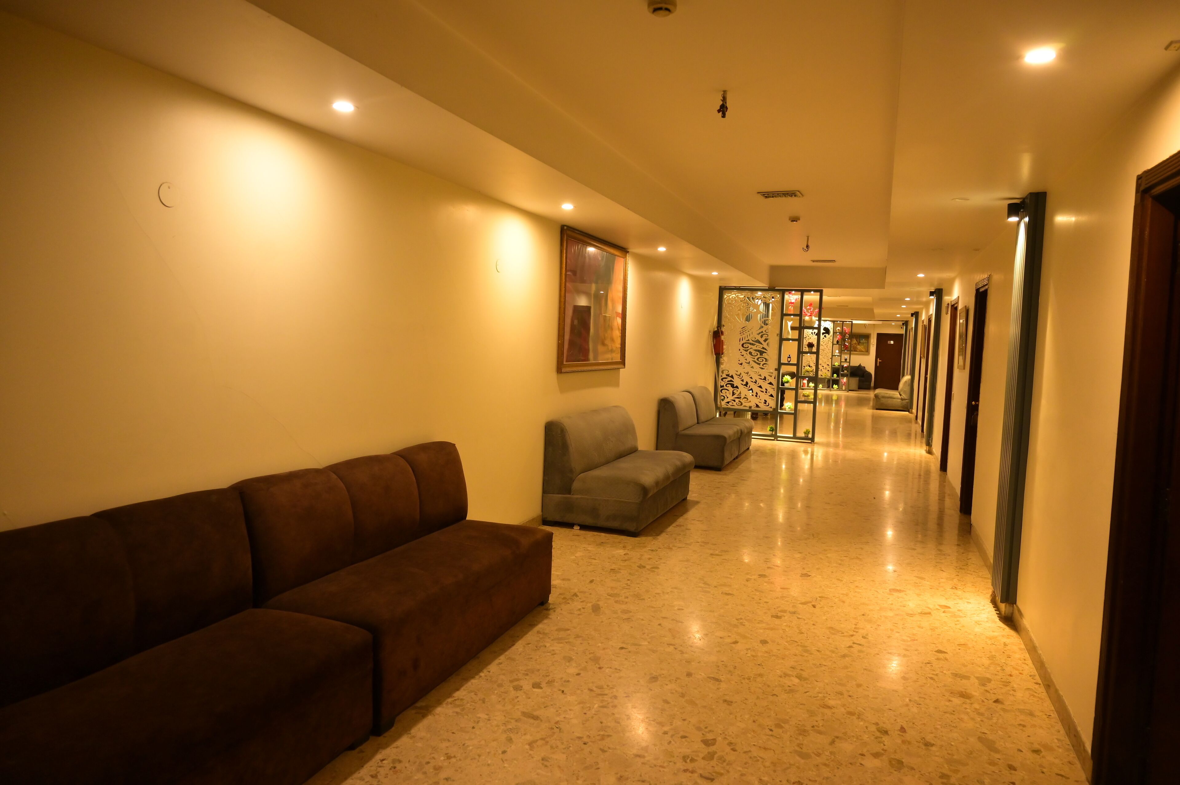 A hotel corridor with a brown sofa, grey armchairs, and a glass partition.