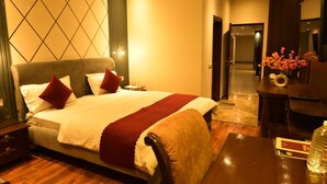 A hotel room with a large bed, bedside tables, a desk with a chair, and a vase with flowers.