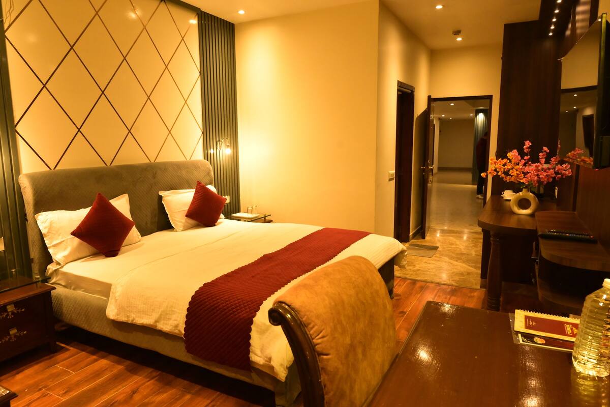 Een hotelkamer met een groot bed, nachtkastjes, een bureau met stoel, en een vaas met bloemen.