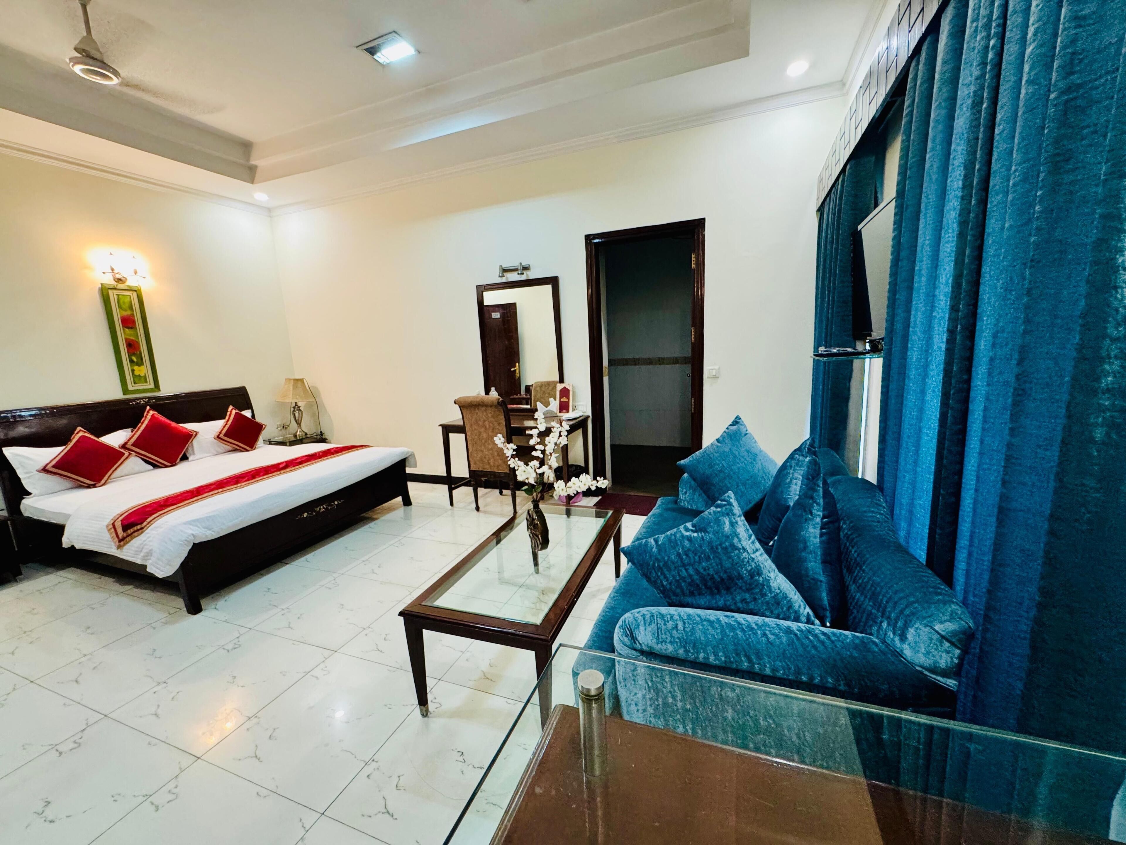 A hotel room with a bed, a sofa, a coffee table, and a mirror.
