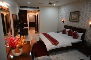 A hotel room with a bed, a desk with a vase of flowers, a chair, a ceiling fan, and a wall-mounted picture.