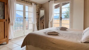 A bedroom with a bed, a wooden wardrobe, and a view of the outdoors through a large window. - Holiday home: Gîte du Levant (Aiglun)