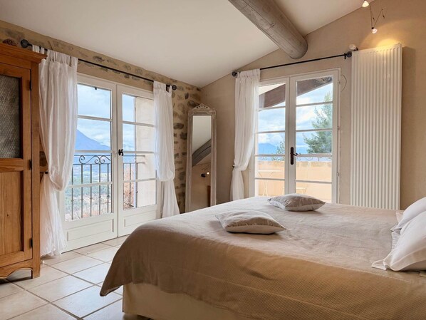A bedroom with a bed, a wooden wardrobe, and a view of the outdoors through a large window.