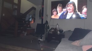 Una sala de estar con una televisión montada en la pared, una escalera, un escritorio y un sofá.
