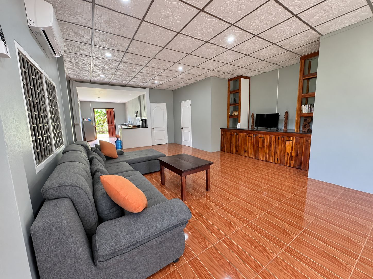 A spacious living area with a grey sectional sofa, a wooden coffee table, and a kitchen in the background.