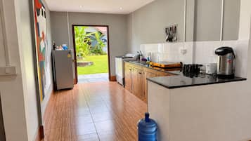 A modern kitchen with a wooden floor, a large water dispenser, and a view of a garden through an open door.
