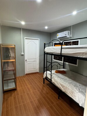 A room with two bunk beds, a wooden shelf unit, a white door, and an air conditioning unit on the wall. - kiwi villas 1 (Vang Vieng)