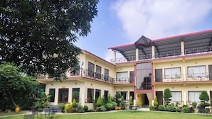 A two-story building with a covered outdoor seating area, multiple windows, and a well-maintained lawn. - Blue River Resort (Ramnagar)