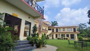 A two-story building with a balcony on the upper floor, a green lawn in front, and a gravel pathway leading to the entrance. - Blue River Resort (Ramnagar)