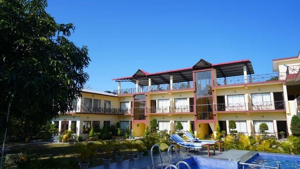 A hotel with a pool, multiple balconies, and a clear blue sky. - Blue River Resort (Ramnagar)