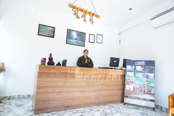 A reception desk with a wooden finish, a hanging decorative piece, framed pictures on the wall, and a promotional poster.