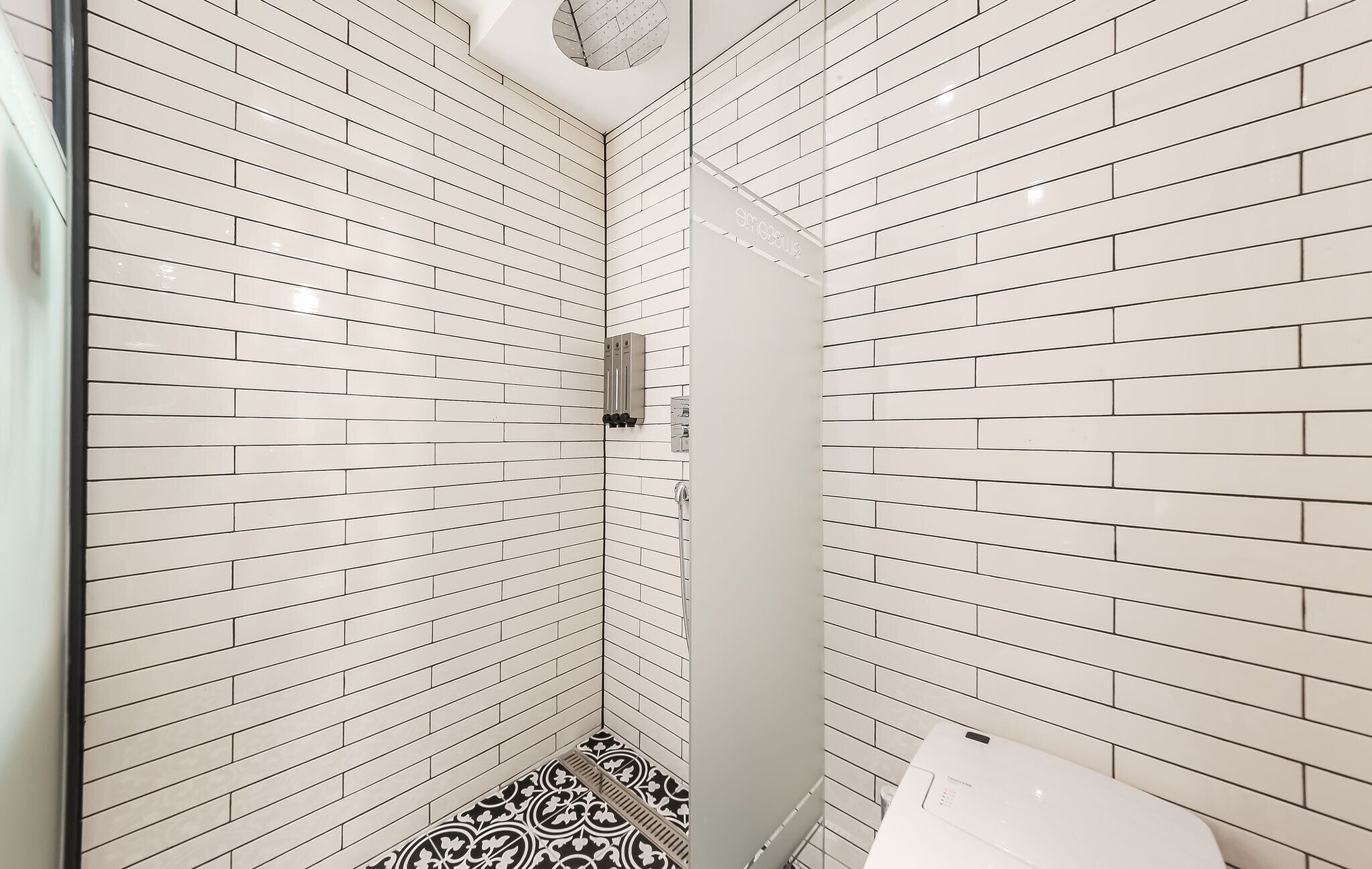 Baño con azulejos blancos estilo metro en paredes y suelo, cabina de ducha de cristal y un inodoro.