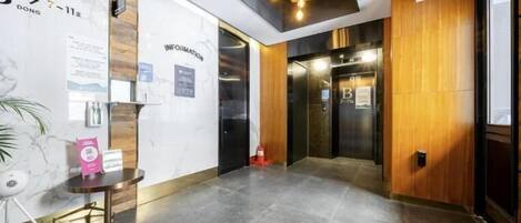 A hotel lobby with a reception desk, information board, and elevators.