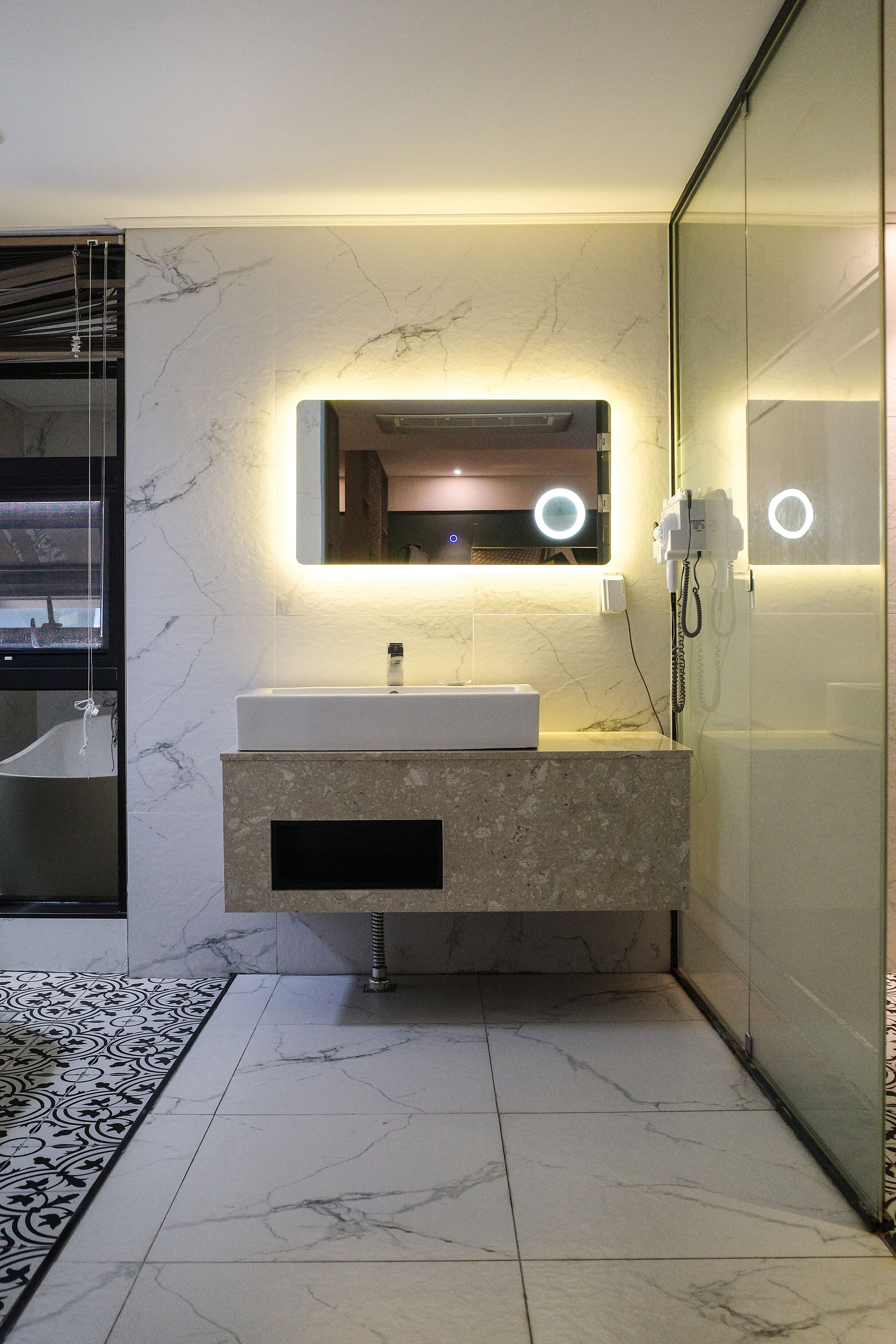 A modern bathroom with a marble sink, a large mirror with integrated lighting, and a glass shower enclosure.