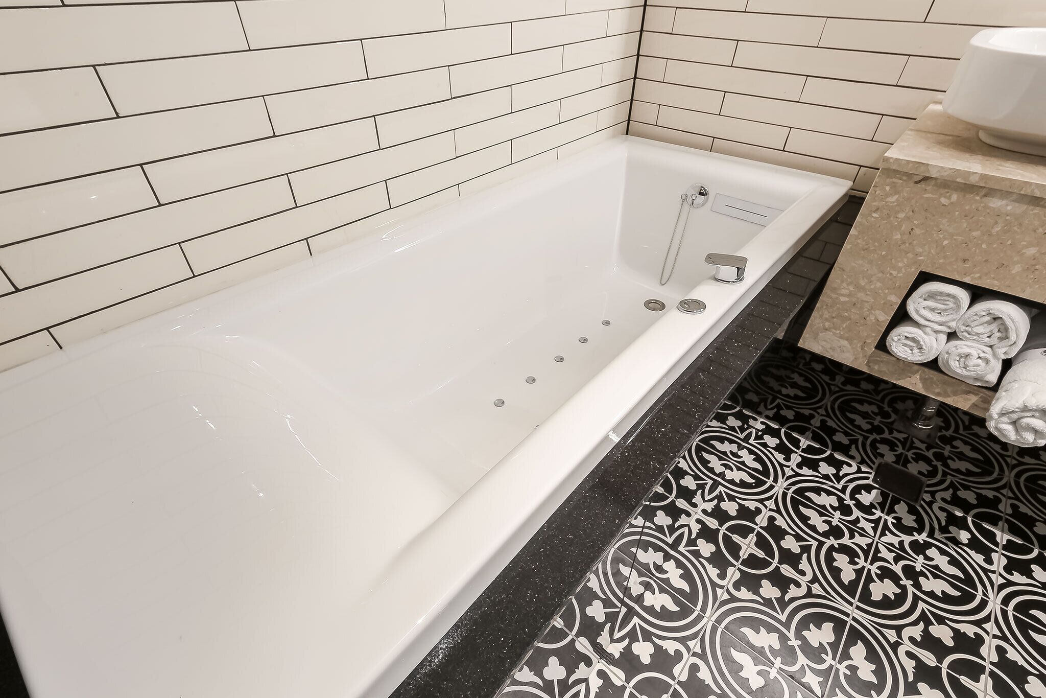A bathroom with a white bathtub, black and white patterned floor tiles, and a towel rack with towels.