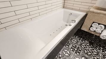 A bathroom with a white bathtub, black and white patterned floor tiles, and a towel rack with towels.