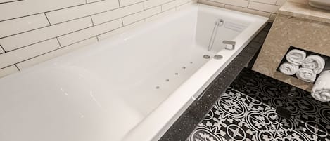 Une salle de bain avec une baignoire blanche, des carreaux de sol à motifs noirs et blancs, et un porte-serviettes avec des serviettes.