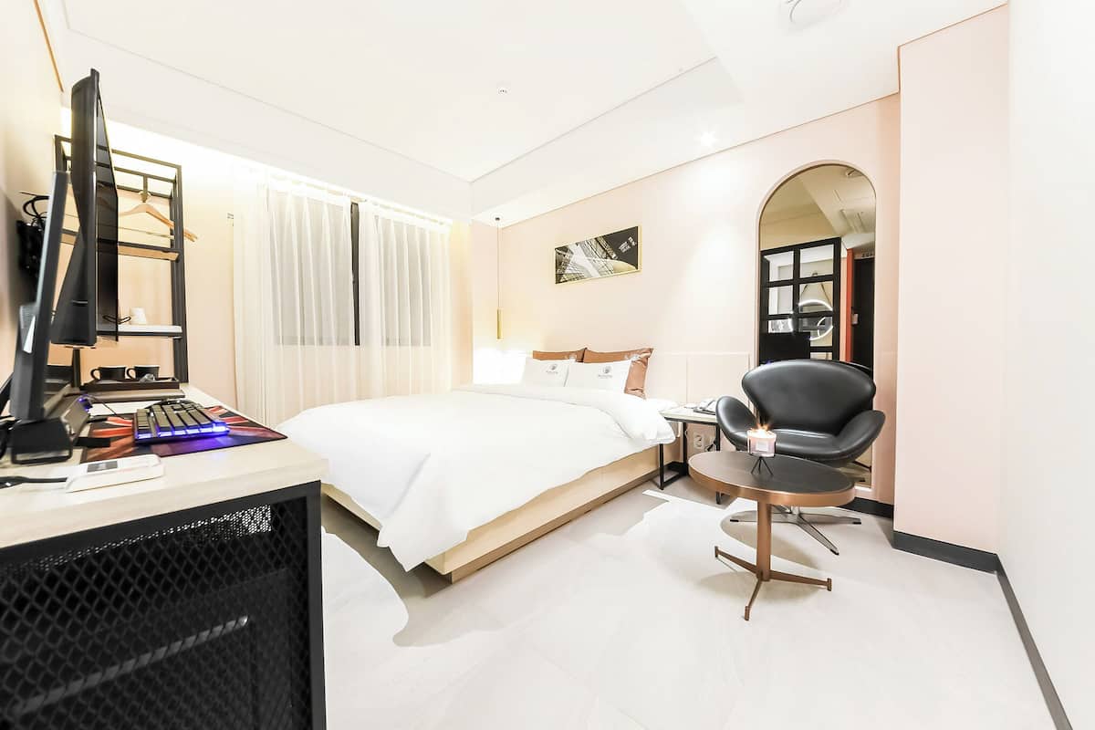 Habitación de hotel con una cama, un escritorio con computadora y teclado, una silla y una lámpara de escritorio.