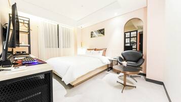 A hotel room with a bed, a desk with a computer and keyboard, a chair, and a desk lamp.